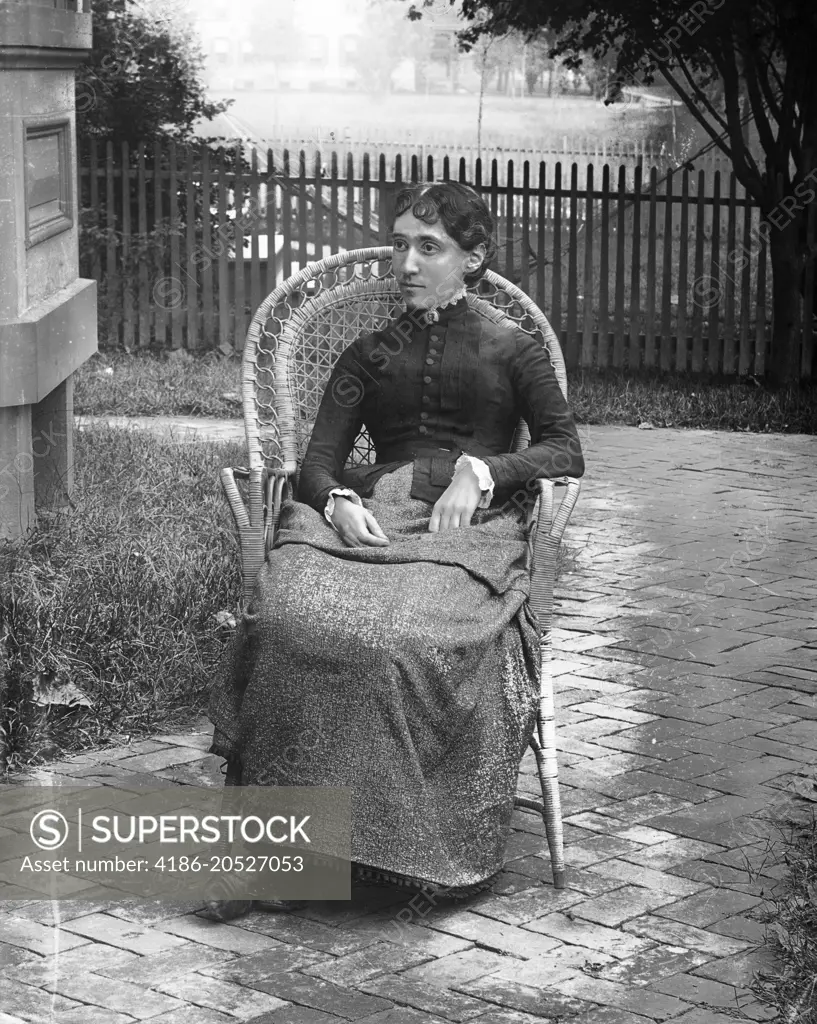 1890s 1900s TURN OF THE 20TH CENTURY PORTRAIT SEVERE WOMAN SITTING IN WICKER CHAIR IN BACKYARD BY HOUSE