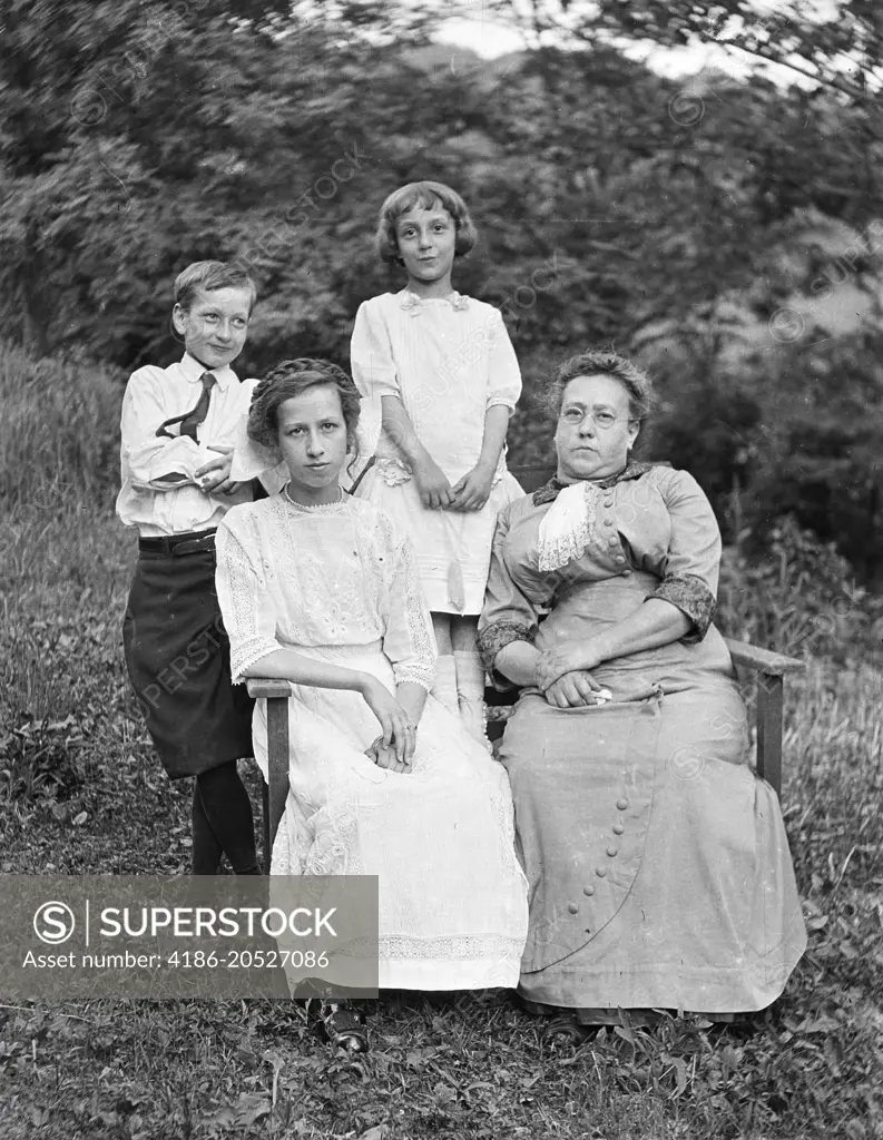 1800s 19TH CENTURY MOTHER AND THREE CHILDREN  SITTING AND STANDING TOGETHER OUTDOORS LOOKING AT CAMERA