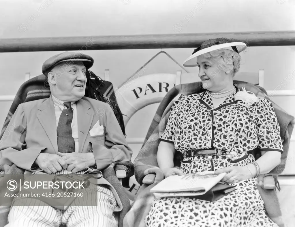 1930s SENIOR COUPLE SITTING IN DECK CHAIRS ON TRANSATLANTIC OCEAN LINER