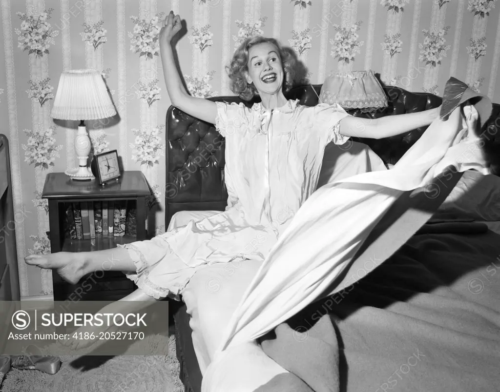 1950s SMILING HAPPY GLEEFUL WOMAN WAKING UP GETTING OUT OF BED FLINGING BACK SHEETS AND BLANKETS