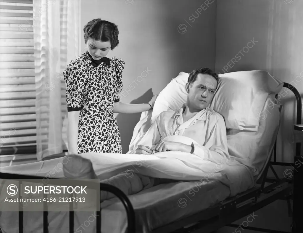 1930s WOMAN BY BEDSIDE MAN IN HOSPITAL BED DEPRESSED WITH BANDAGED LEG