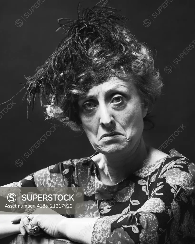 1970s PORTRAIT SENIOR WOMAN WITH MEAN SOUR SAD ANGRY FACIAL EXPRESSION WEARING A FEATHERED HAT LOOKING AT CAMERA