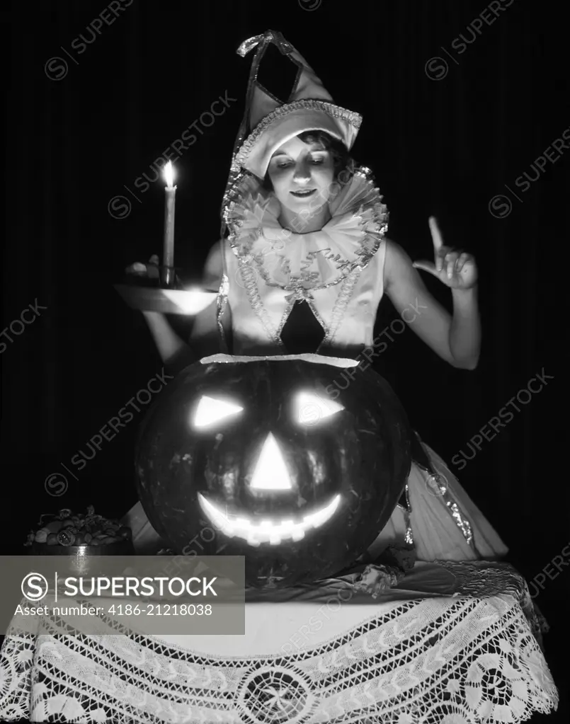 1920s 1930s WOMAN IN HARLEQUIN COSTUME HOLDING CANDLE LOOKING DOWN INTO CARVED PUMPKIN JACK-O-LANTERN 