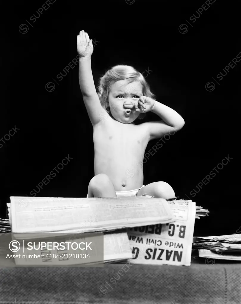 1940s LITTLE BLOND TODDLER GIRL IMITATING HITLER GIVING NAZI SALUTE SITTING ON PILE OF NEWSPAPERS