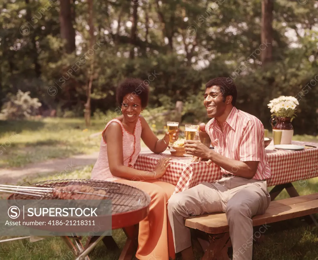 1970s SMILING AFRICAN AMERICAN COUPLE MAN WOMAN DRINKING BEER AT BACKYARD BARBECUE