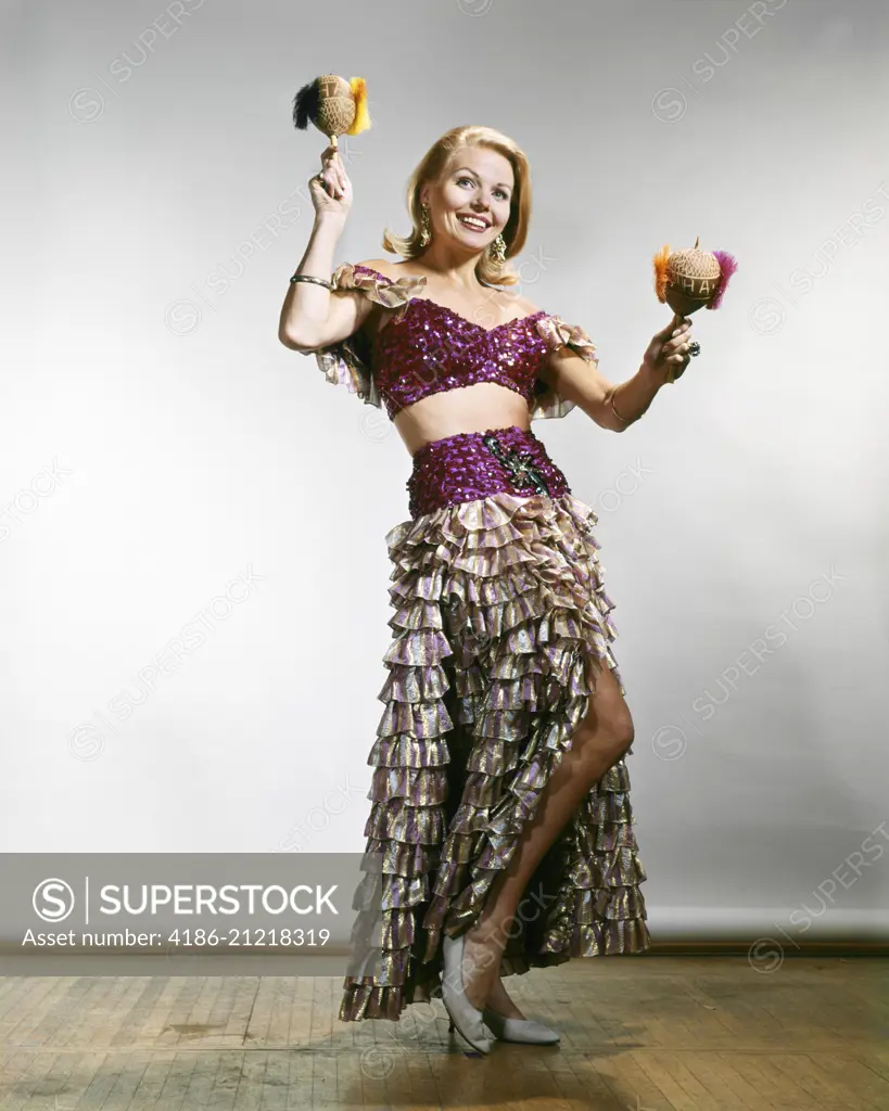 1960s FULL LENGTH BLONDE WOMAN CALYPSO CARIBBEAN COSTUME WITH BARE MIDRIFF SHAKING MARACAS LOOKING AT CAMERA