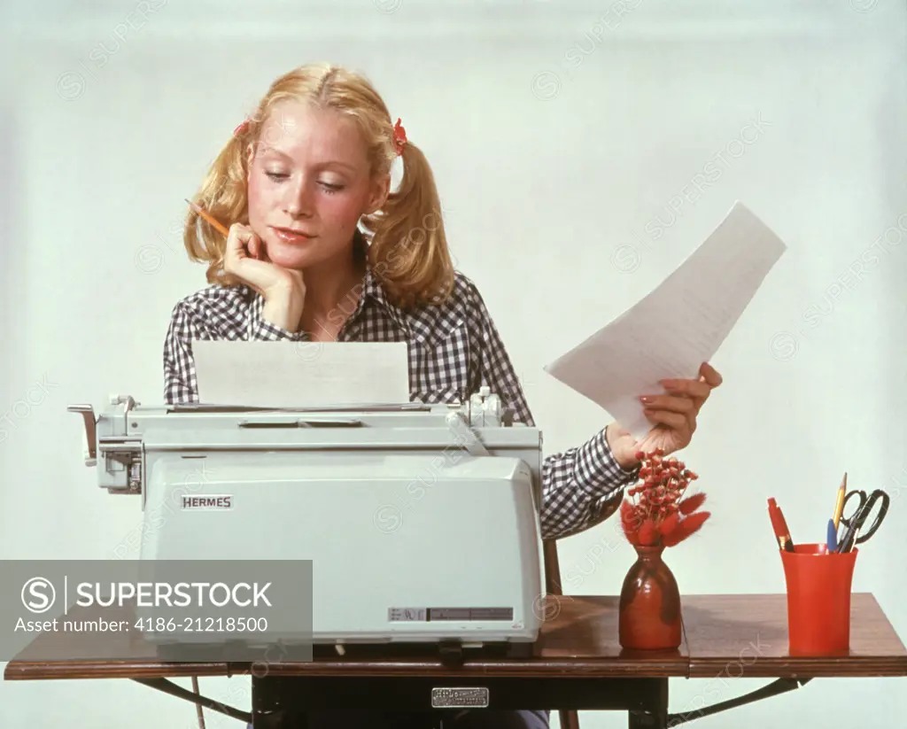 1970s YOUNG WOMAN BLONDE HAIR AT ELECTRIC HERMES TYPEWRITER THOUGHTFUL PENSIVE STUDENT TYPING WEARING HAIR IN PIGTAILS 