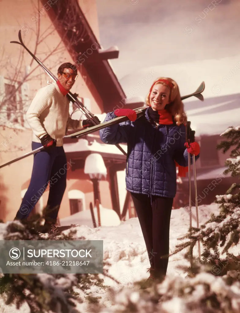 1970s COUPLE MAN WOMAN HOLDING SKIS SKI POLES SKI CHALET LODGE SNOW PINE TREES CLOTHES FASHION LIFESTYLE