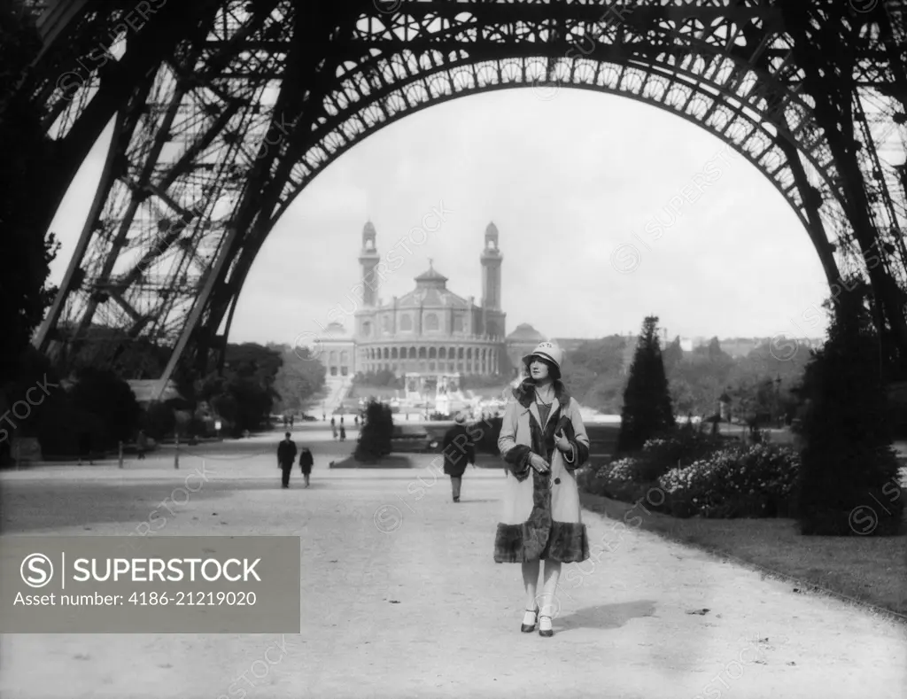 1920s WOMAN WALKING UNDER THE EIFFEL TOWER WITH THE TROCADERO IN BACKGROUND PARIS FRANCE 