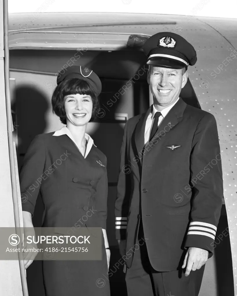 1960s MAN CO-PILOT AND WOMAN FLIGHT ATTENDANT STANDING SMILING IN DOOR OF AIRPLANE LOOKING AT CAMERA 