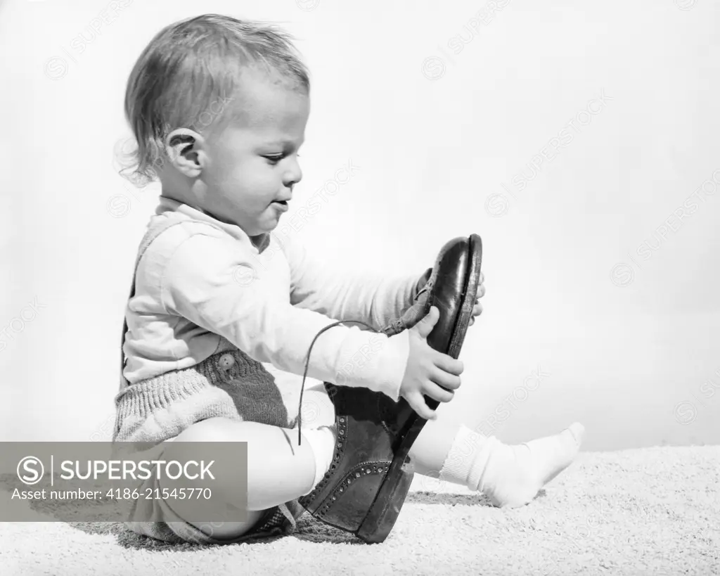 1960s BABY BOY TRYING TO PUT ON ADULT MAN'S SHOE