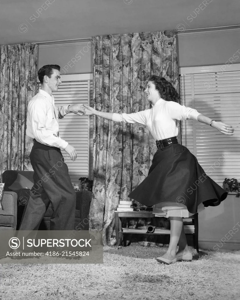 1950s TEEN BOY AND GIRL JITTERBUG DANCING TO ROCK AND ROLL MUSIC IN LIVING ROOM 