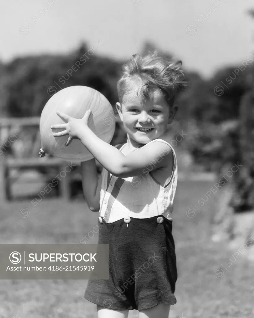 1930s SMILING BOY SUMMER OUTDOOR PLAYING IN BACKYARD LOOKING AT CAMERA READY TO TOSS BALL 