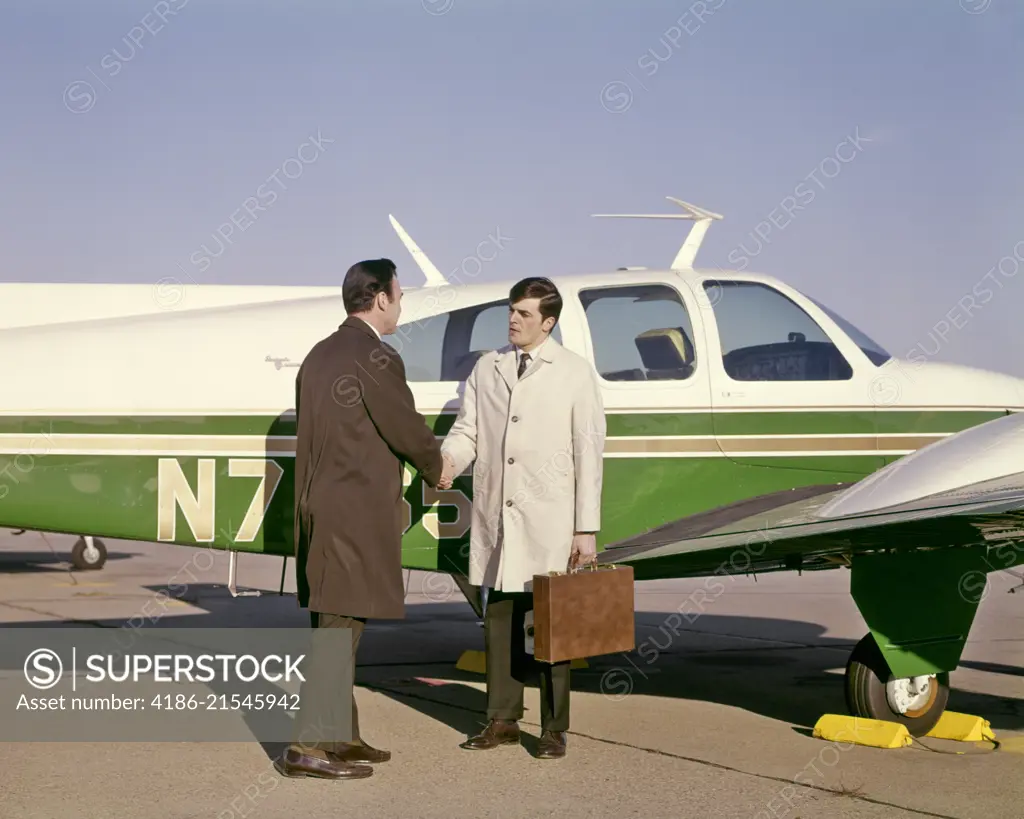 1960s TWO BUSINESS MEN SHAKING HANDS STANDING BESIDE SMALL PRIVATE AIRPLANE