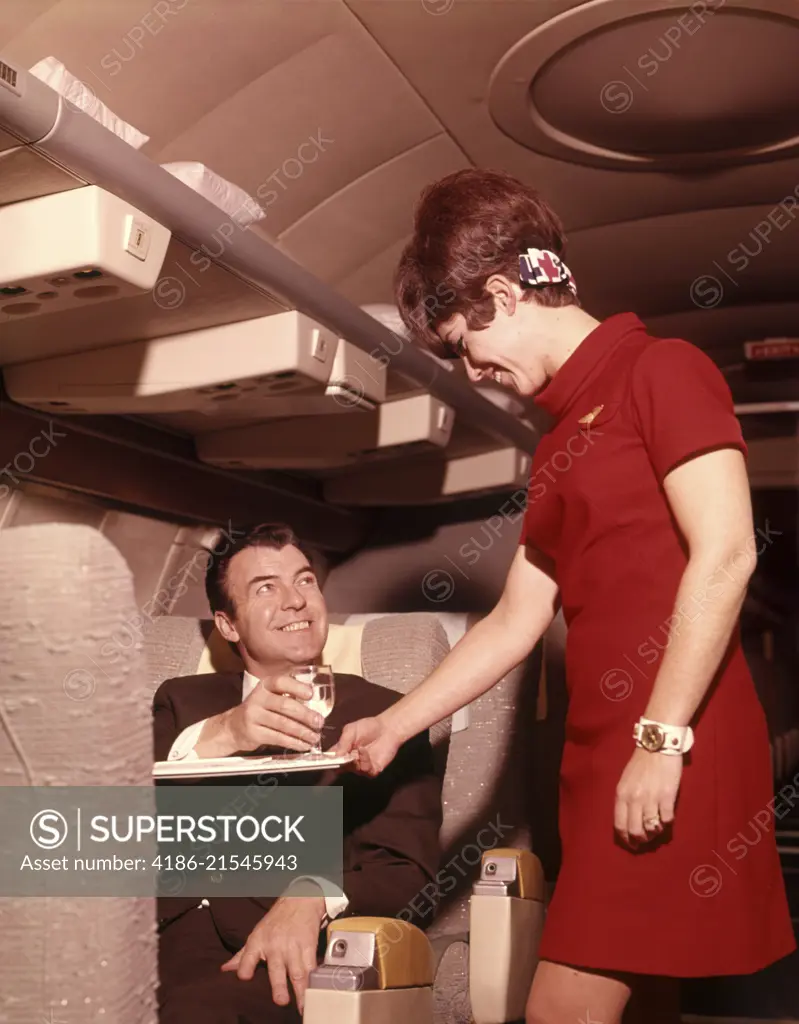 1960s 1970s AIRPLANE PLANE STEWARDESS SERVING BUSINESS MAN DRINK WINE WOMAN COMMERCIAL AIR TRAVEL