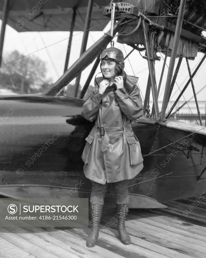 1920s FEMALE AVIATOR AVIATRIX LEATHER COAT CAP WITH GOGGLES AND LACE UP BOOTS PREPARING TO BOARD SEAPLANE