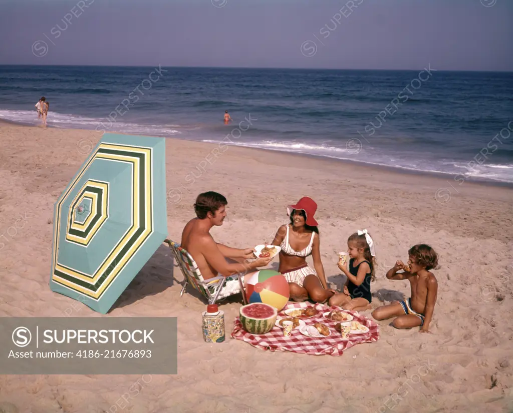 1970s FAMILY EATING PICNIC AT OCEAN BEACH 