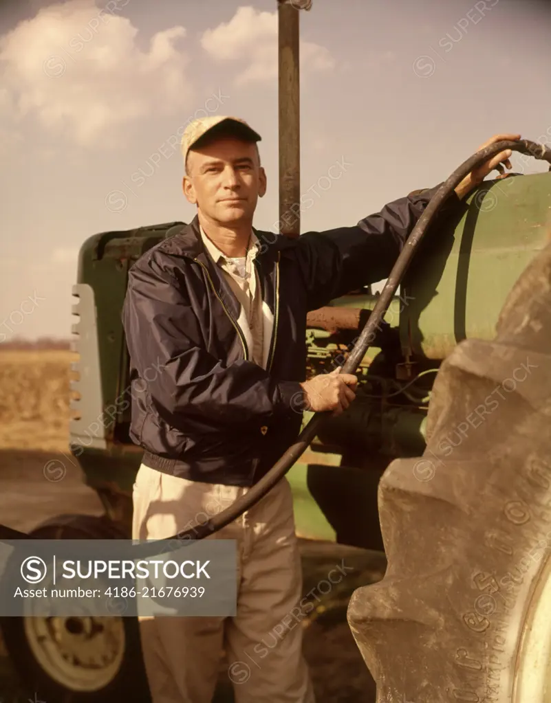 1960s PORTRAIT OF SERIOUS MAN FARMER LOOKING AT CAMERA FUEL INTO TRACTOR