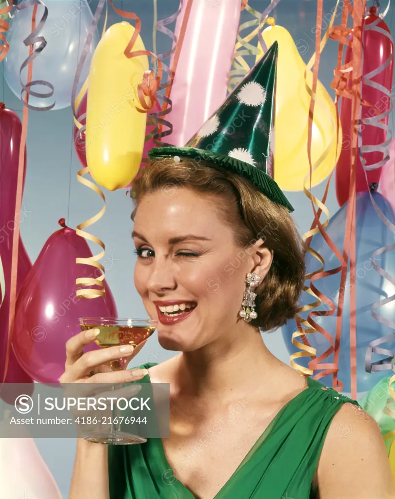 1960s BLOND WOMAN CELEBRATING NEW YEARS WEARING PARTY PAPER HAT DRINKING CHAMPAGNE LOOKING AT CAMERA WINKING EYE