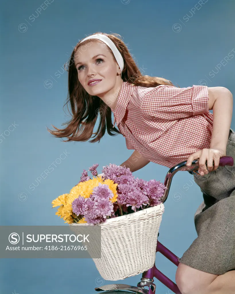 1960s REDHEAD WOMAN RIDING BICYCLE WITH BASKET FULL OF AUTUMN FLOWERS