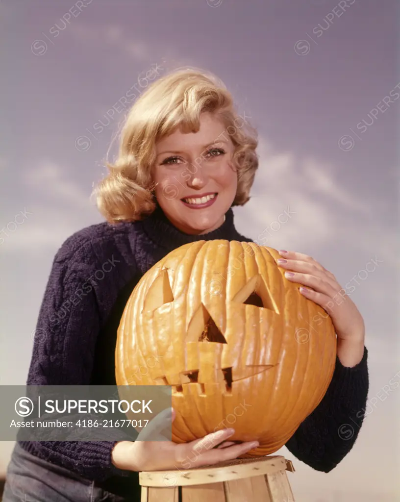 1960s SMILING BLOND WOMAN HOLDING JACK-O-LANTERN CARVED PUMPKIN LOOKING AT CAMERA