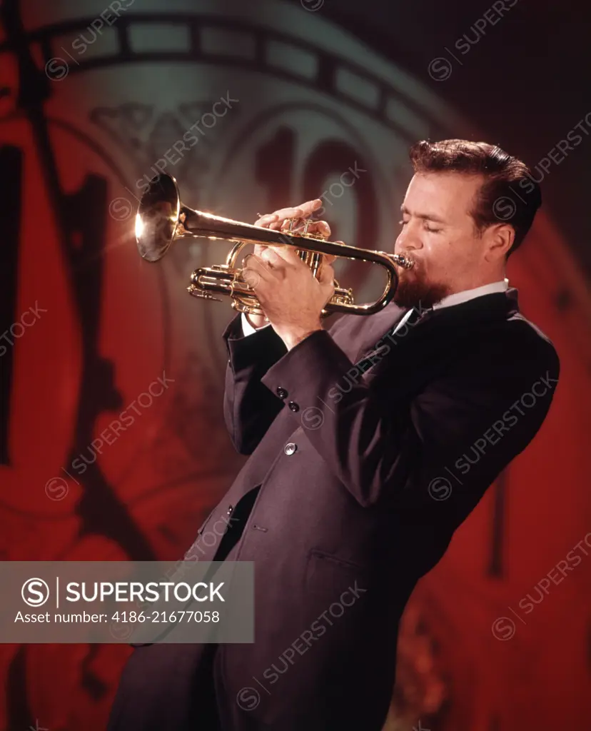 1960s MAN JAZZ MUSICIAN PLAYING TRUMPET NEAR MIDNIGHT NEW YEARS CLOCK FACE IN BACKGROUND