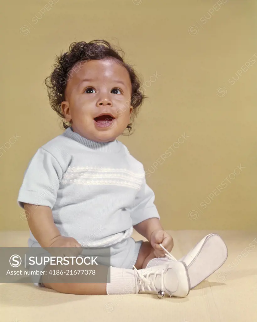 1970s SMILING CURLY HAIR AFRICAN AMERICAN BABY BOY SITTING HAPPY LOOKING UPWARD