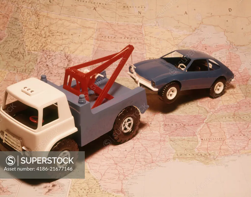 1970s TOY TOW TRUCK TOWING TOY CAR ACROSS PRINTED ROAD MAP BACKGROUND SYMBOLIC AUTOMOBILE ROAD SERVICE REPAIR