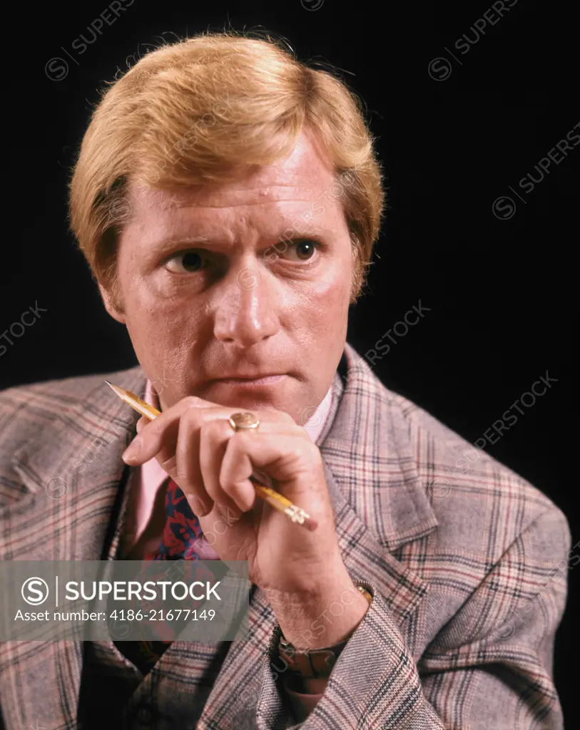 1970s BLOND BUSINESSMAN WITH AMBIGUOUS FACIAL EXPRESSION WEARING THREE PIECE PLAID SUIT HOLDING PENCIL