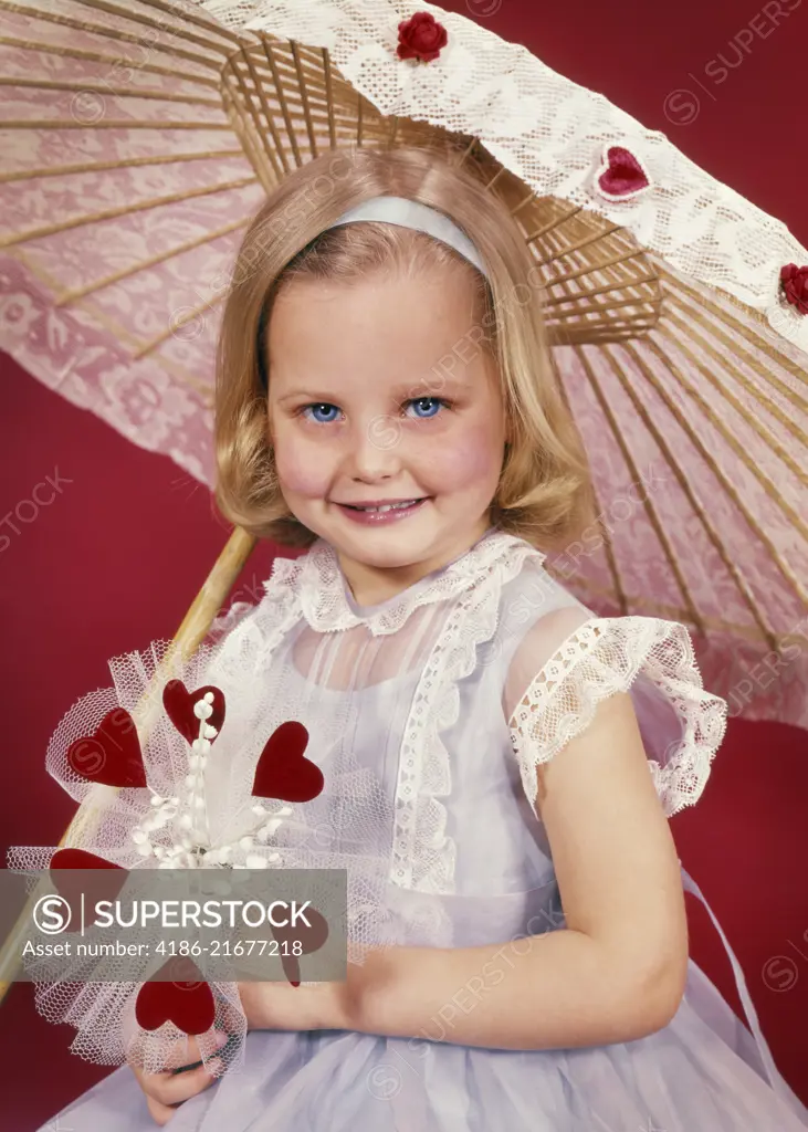 1950s SMILING LITTLE BLOND GIRL LOOKING AT CAMERA WITH VALENTINE BOUQUET OF RED HEARTS AND FLOWERS UNDER LACY PARASOL UMBRELLA