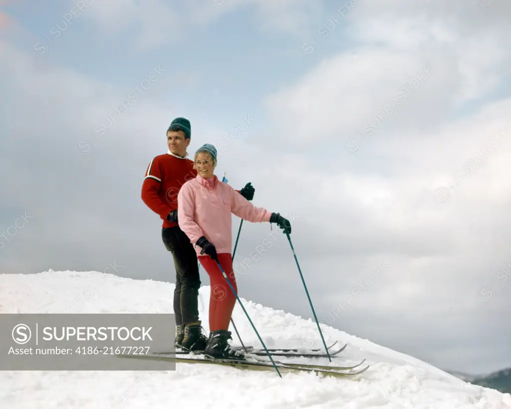 1960s COUPLE POSED TOP SNOWY HILL WOMAN PINK SWEATER RED SKI PANTS MAN RED SWEATER SKIS SKIING SPORTS VERMONT USA