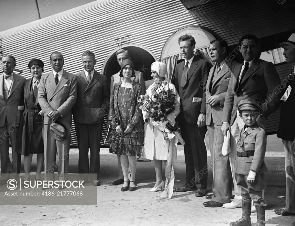 1920s AVIATOR CHARLES LINDBERGH AND HIS WIFE ANNE STANDING BY AIRPLANE WITH GROUP OF PEOPLE ON INAUGURAL FLIGHT OF TAT AIRLINE