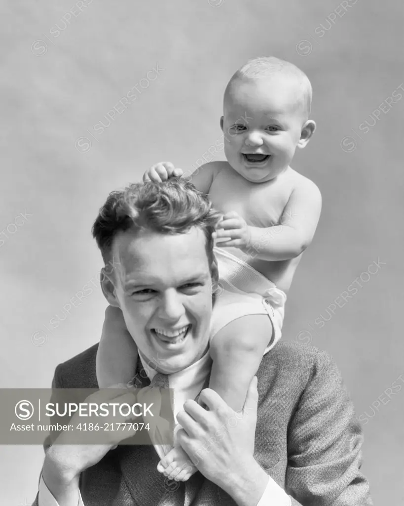 1930s LAUGHING FATHER CARRYING BABY SON ON HIS SHOULDERS AS KID PULLS DAD'S HAIR