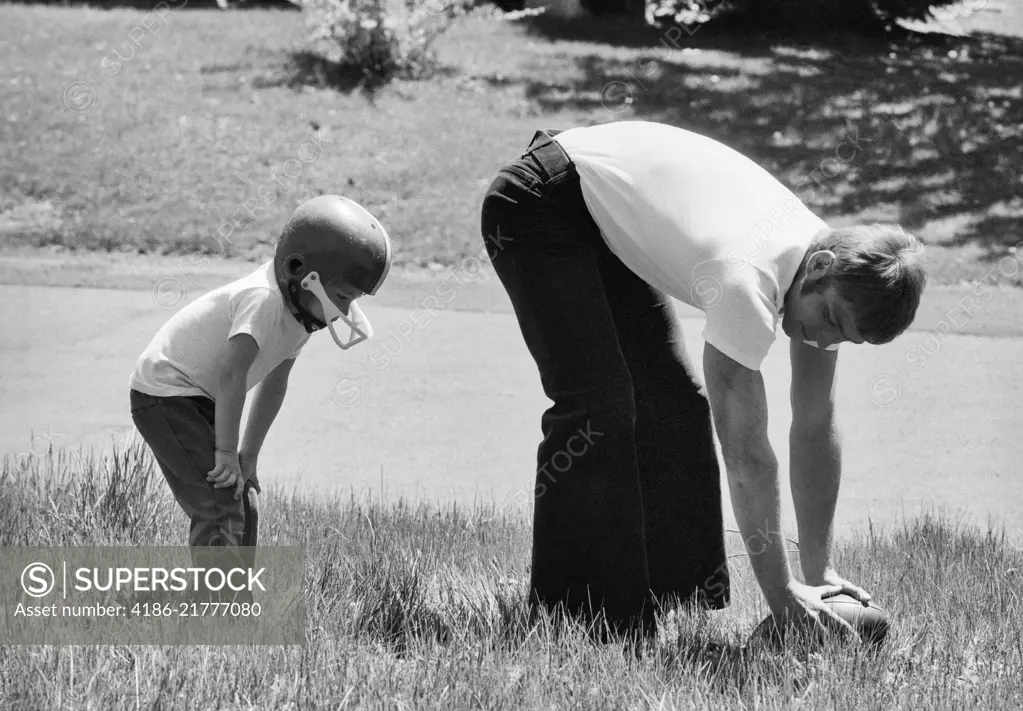 1970s FATHER PLAYING FOOTBALL ON GRASS IN WITH YOUNG SON 