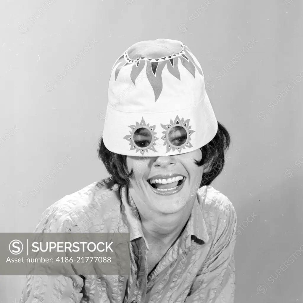 1960s SMILING WOMAN WEARING FUNNY WACKY SUN HAT WITH SUNSPOTS FOR EYEGLASSES LOOKING AT CAMERA