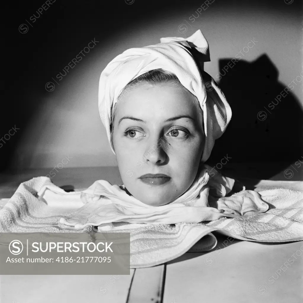 1950s PORTRAIT HEAD SHOT OF WOMAN RELAXING IN SPA SAUNA STEAM CABINET TOWEL WRAPPED AROUND HEAD