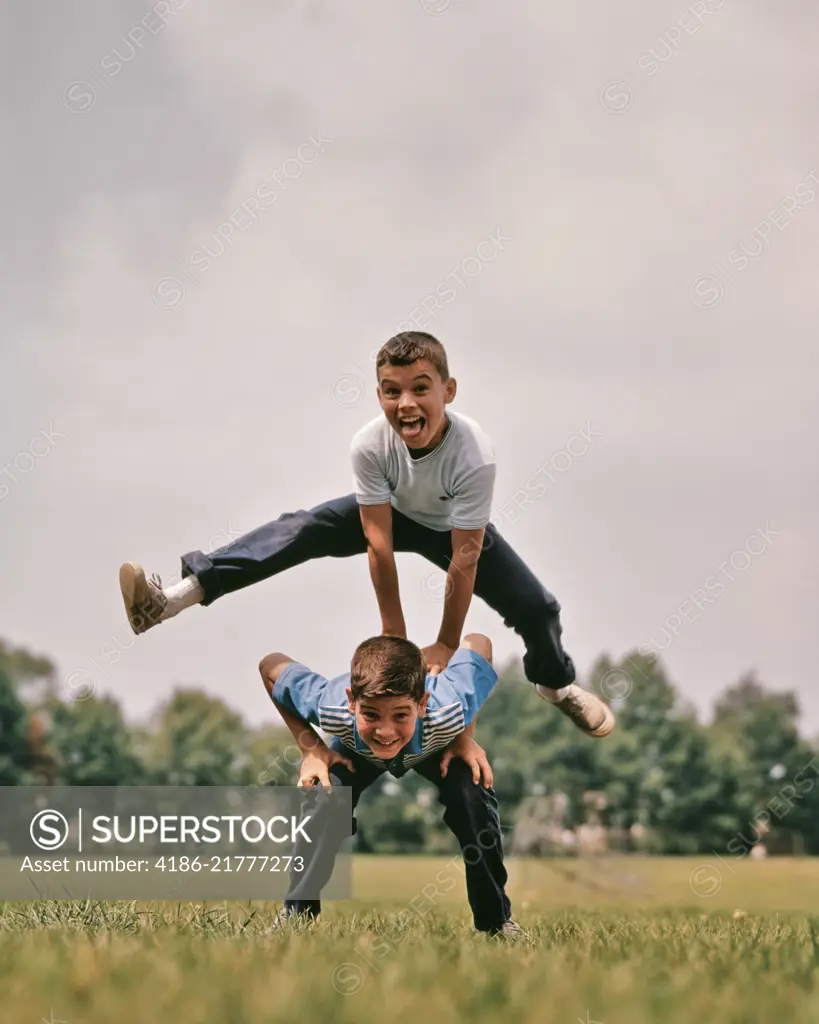 1960s BOYS PLAYING LEAP FROG ONE JUMPING OVER THE OTHER'S BACK LOOKING AT CAMERA