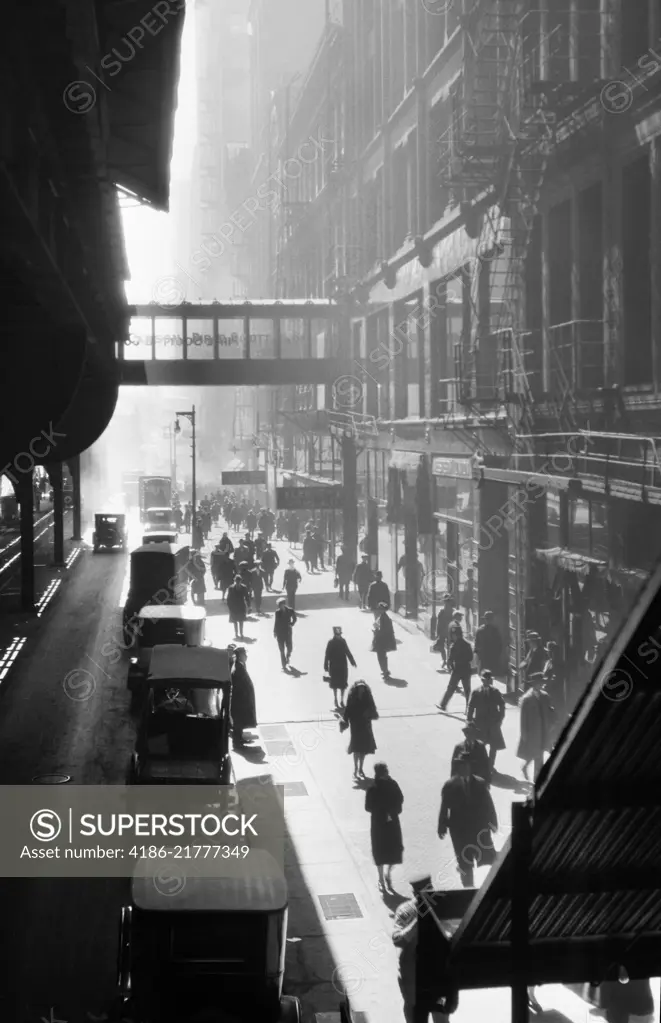 1970s ANONYMOUS SILHOUETTED PEDESTRIANS WALKING ON SIDEWALK WITH CARS PARKED ALONG CURB BENEATH ELEVATED TRAIN NEW YORK CITY USA