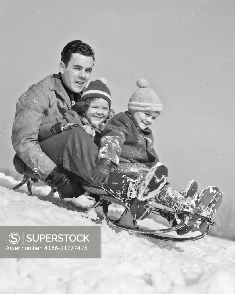 1930s 1940s FATHER TWO CHILDREN ON SLED IN SNOW GOING DOWN HILL