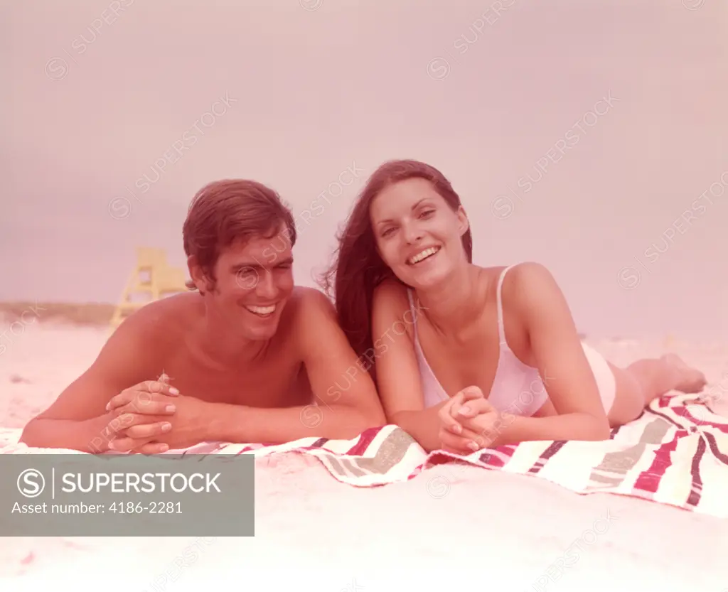 1960S Smiling Young Couple Lying Side By Side Together On Beach Towel