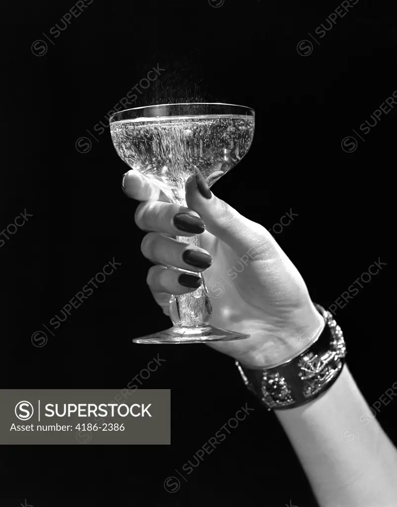 1930S 1940S 1950S Woman Hand Ornate Metal Bracelet Holding Up New Year Toast Glass Of Champagne Against Black Background