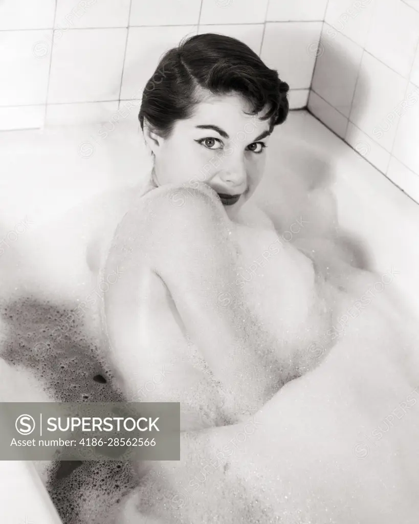 1950s 1960s PRETTY BRUNETTE YOUNG WOMAN IN BATHTUB TAKING BUBBLE BATH LOTS  OF SUDS SEXY LOOKING AT CAMERA OVER HER BARE SHOULDER - SuperStock