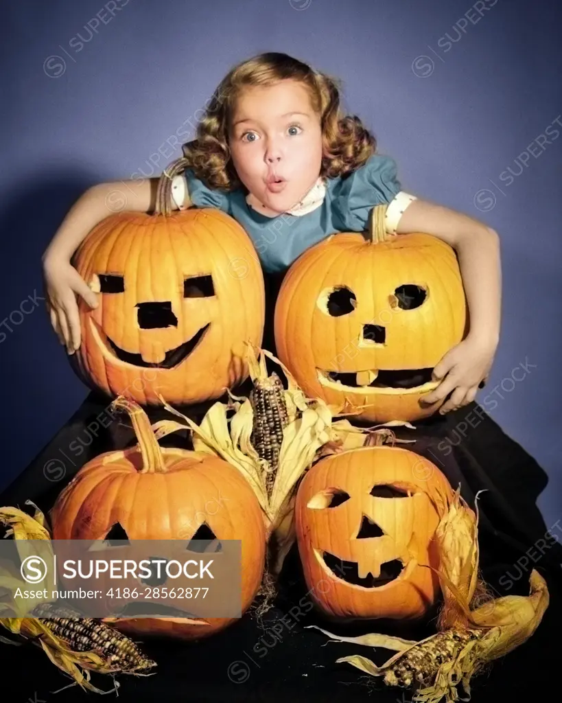 1950s LITTLE GIRL STANDING ABOVE FOUR CARVED HALLOWEEN PUMPKINS JACK-O-LANTERNS WITH SCARED FACIAL EXPRESSION LOOKING AT CAMERA