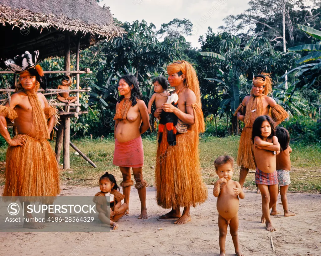 1960s YAGUAS INDIANS OF THE UPPER AMAZON BASIN MEN IN GRASS SKIRTS TOPLESS  WOMAN AND NAKED CHILDREN NEAR IQUITOS PERU - SuperStock