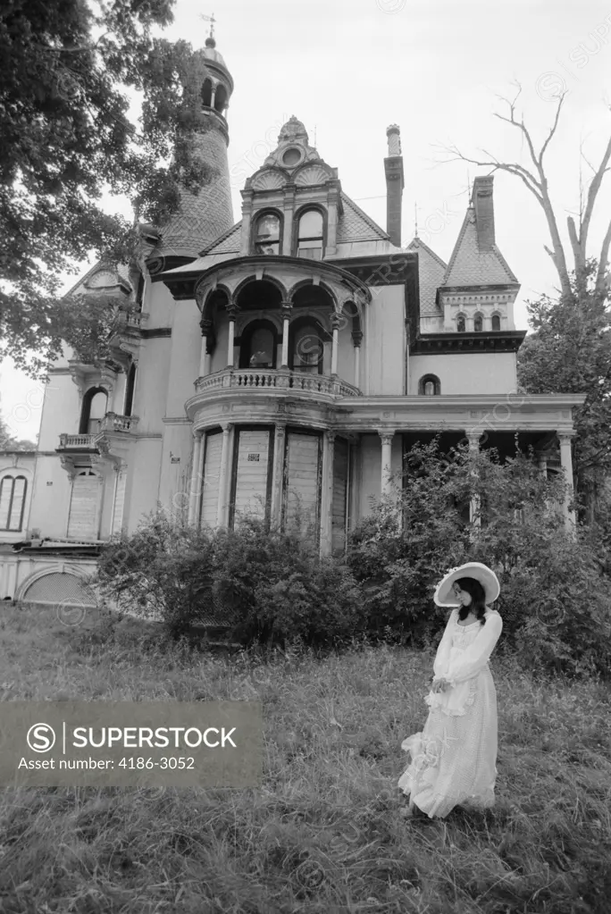 Woman In Victorian Costume Standing On Front Lawn Of Large Abandoned Haunted Victorian Home