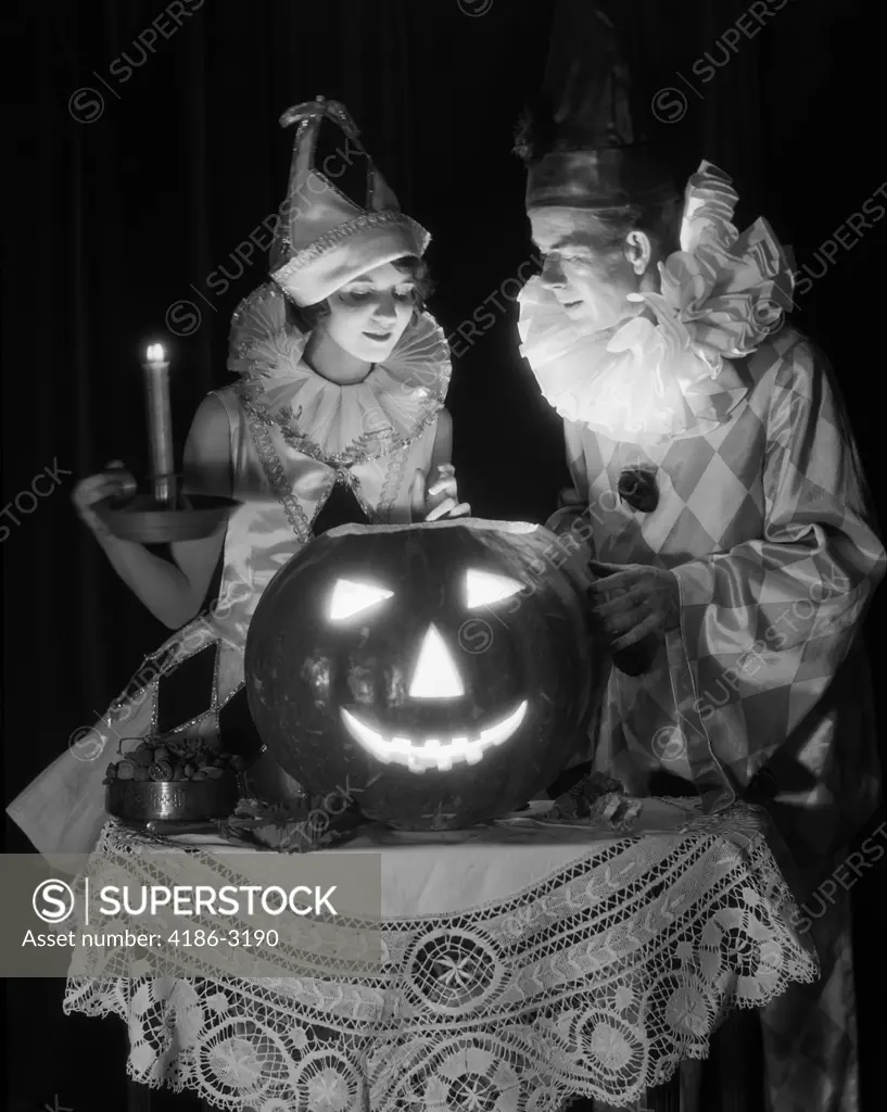 1920S 1930S Couple In Costumes Looking Down Into Candle Light From Carved Pumpkin Jack-O-Lantern