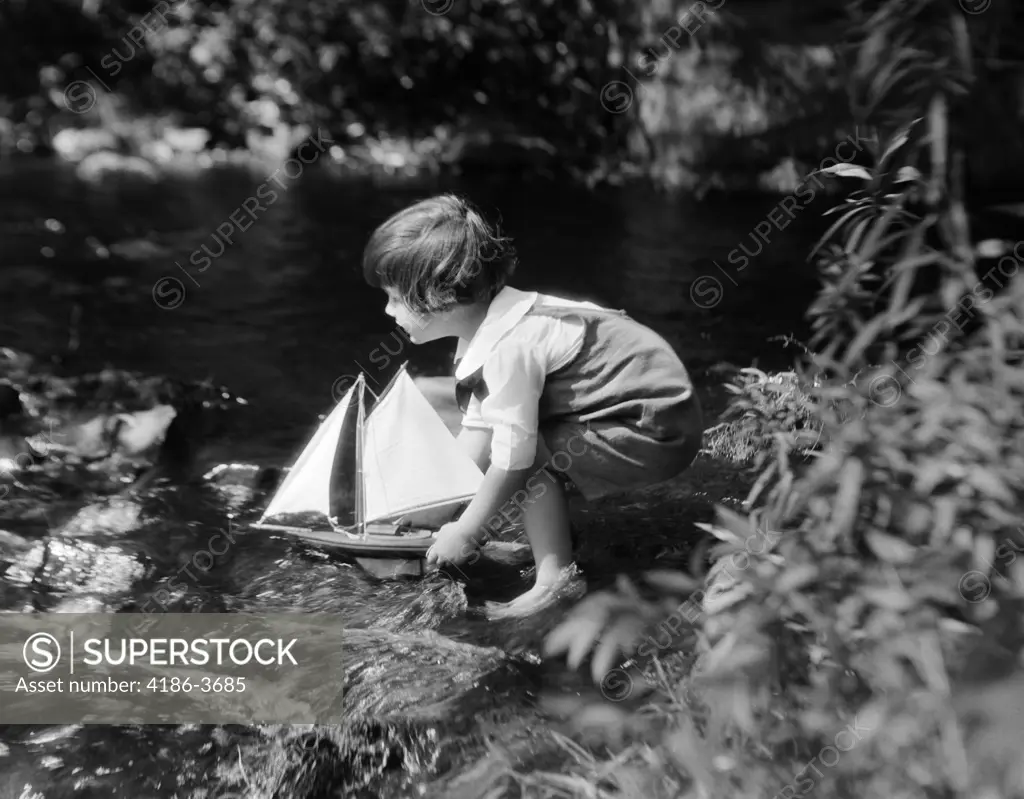 1920S Boy Putting Toy Sailboat Into Stream