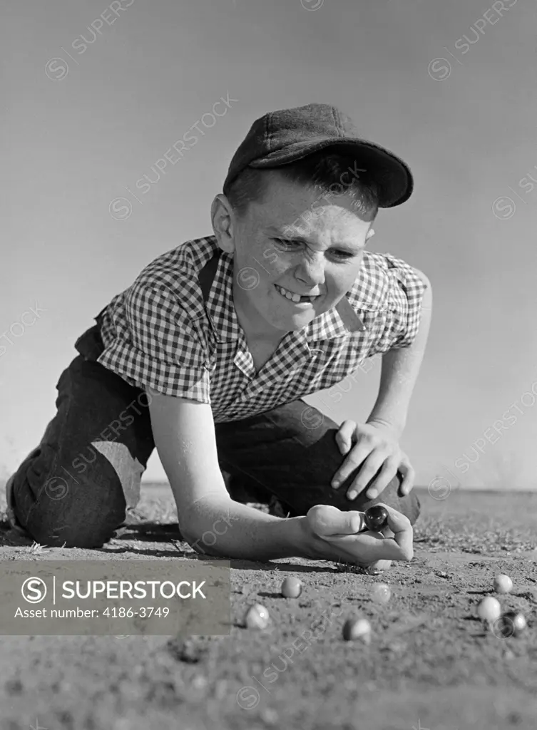 1950S 1960S Boy Playing Marbles Kneeling In The Dirt Squinting Missing A Front Tooth