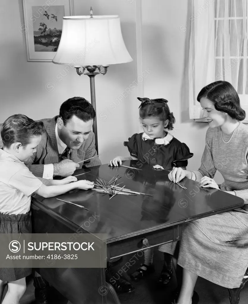 1940S Parents Playing Pick Up Sticks Game With Young Son And Daughter Indoor