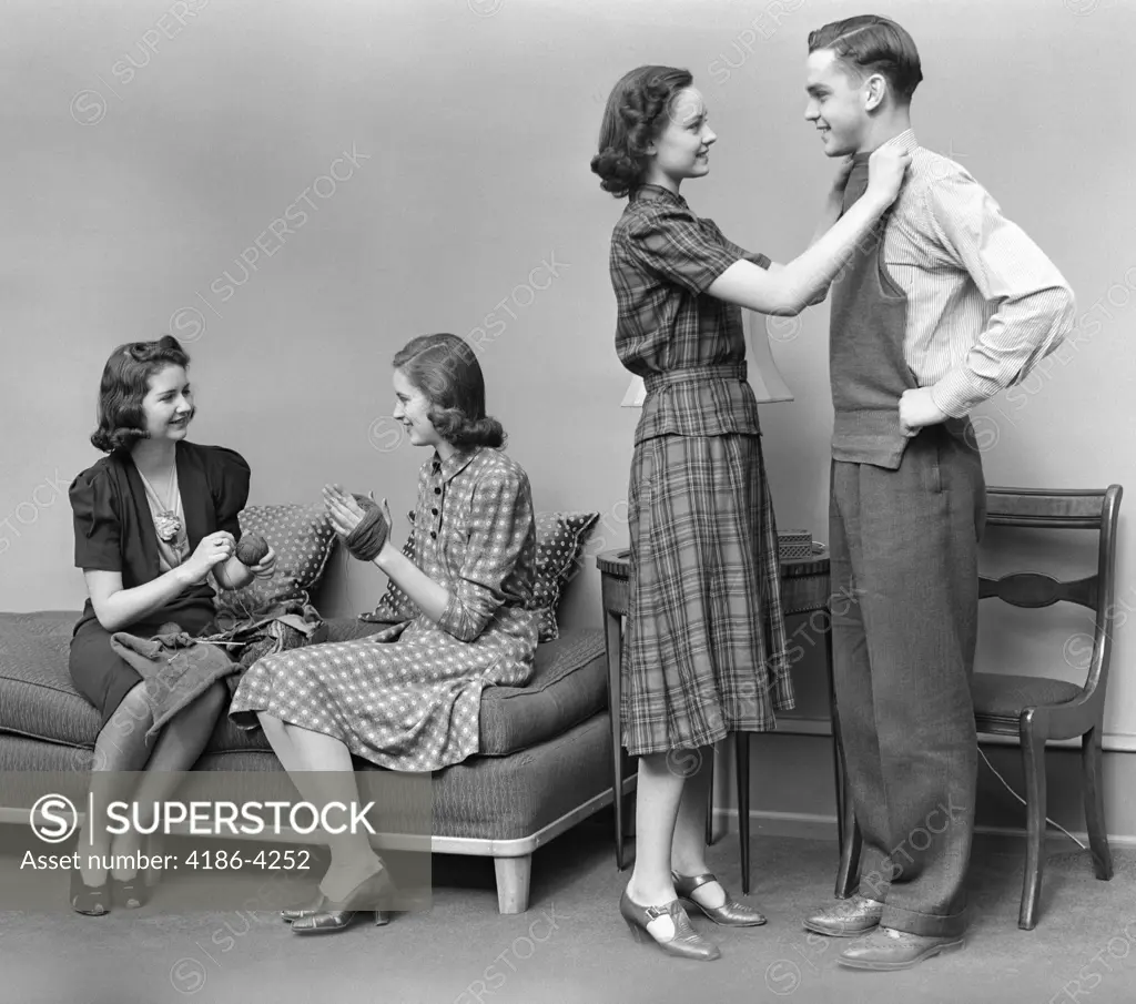 1940S Teen Group Two Girls Unwind Skein Yarn Another Girl Holds Knitted Vest Up To Fit On Boy